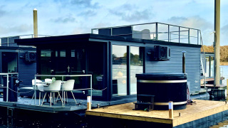 Moderne woonboot bij Marina Mookerplas met dakterras en buitenspa, drijvend op rustig water.