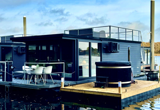 Moderne woonboot bij Marina Mookerplas met dakterras en buitenspa, drijvend op rustig water.