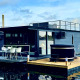 Modern houseboat at Marina Mookerplas with a rooftop terrace and outdoor hot tub, floating on calm water.