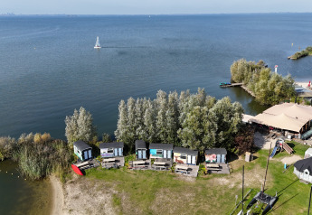 Luftfoto af små hytter ved søbredden i Marina Parcs Almere, Holland, omgivet af grønne træer og vand.