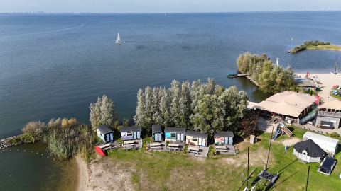 Vista aerea delle tiny house sul lago a Marina Parcs Almere, Paesi Bassi, circondate da alberi e acqua.