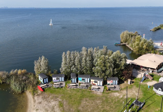 Vista aerea delle tiny house sul lago a Marina Parcs Almere, Paesi Bassi, circondate da alberi e acqua.