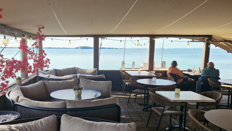 Terraza acogedora con cómodos asientos y vista al agua, donde dos personas disfrutan del paisaje.