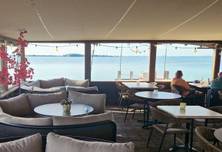 Knus terras met comfortabele zitplaatsen en uitzicht op het water, waar twee mensen genieten.