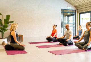 Eine Gruppe praktiziert Yoga in einem kleinen Haus mit hellen Fenstern und minimalistischer Einrichtung.