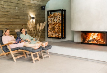 Two people relax on lounge chairs by a fireplace in a cozy glamping accommodation with wood decor.