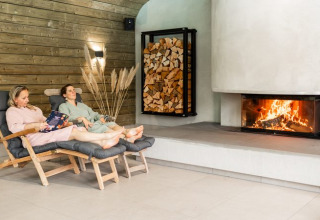 Dos personas se relajan en sillas frente a una chimenea en un alojamiento de glamping acogedor.