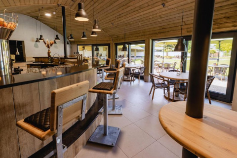 Zona bar e caffetteria moderna con arredi in legno e grandi vetrate in un glamping con area esterna.