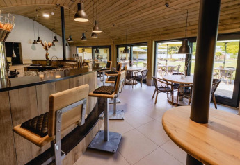 Zona bar e caffetteria moderna con arredi in legno e grandi vetrate in un glamping con area esterna.