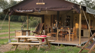 Tenda safari con doccia privata, veranda in legno e tavolo da picnic a De Oude Melkstal, Paesi Bassi.