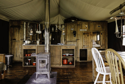 Interieur van een rustieke safaritent met houten meubilair en houtkachel bij Feather Down De Oude Melkstal.