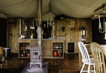 Interior view of a rustic safari tent with wooden furnishings and wood stove at Feather Down De Oude Melkstal.