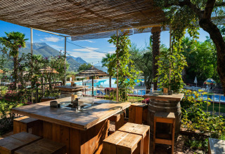 Gemütlicher Essbereich im Freien mit Holz- und Fassmöbeln am Pool im Weekend Glamping Resort, Lombardei.