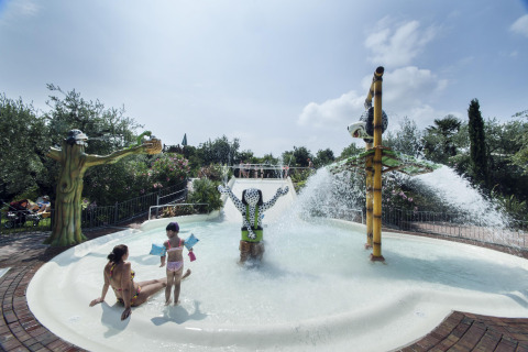 Children and an adult play in a splash pool with water features and statues at Weekend Glamping Resort, Lombardy.