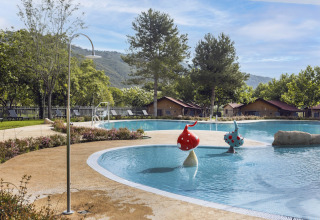 Außenpool mit Pilzfiguren, Liegestühlen und Hütten im Hintergrund im Wecamp Pirineos, Aragonien, Spanien.