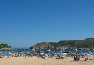 Strandbeeld bij Wecamp L'Escala Punta Mila in Catalonië, Spanje met bezoekers, parasols en boten op zee.