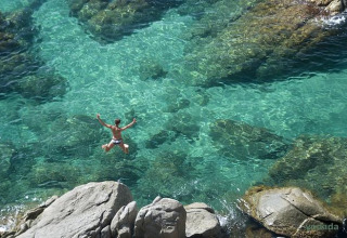 Person jumping off rocks into clear turquoise water at Wecamp L'Escala Punta Mila in Catalonia, Spain.
