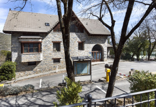 Stenen gebouw met zadeldak en parkeerplaats bij Wecamp Pirineos vakantiepark in Aragón, Spanje, tussen bomen.