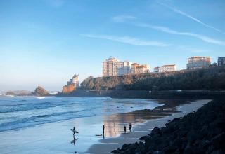Surfers on a beach near San Sebastián in Basque Country, Spain, with rocky shore and buildings in the background.