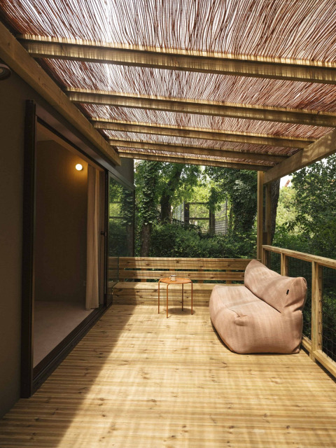 Terraza de madera con sofá cómodo y mesa bajo techo sombreado en Wecamp San Sebastián, País Vasco, España.