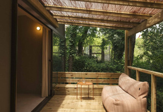 Wooden terrace with cozy lounger and table under shaded roof at Wecamp San Sebastián, Basque Country, Spain.