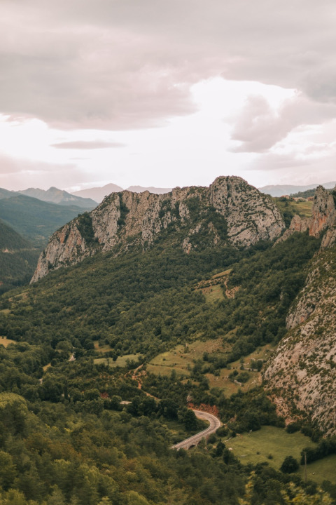 Uitzicht op groene bergen en een kronkelende weg bij WeCamp Pirineos, vakantiekamp in Aragón, Spanje bij bewolkte lucht.