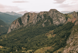 Blick auf grüne Berge und kurvige Straßen im Ferienpark WeCamp Pirineos, Aragón, Spanien unter bewölktem Himmel.
