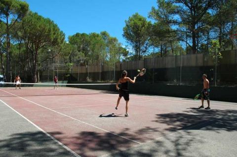 Cuatro personas juegan al tenis en una pista al aire libre rodeada de árboles en Wecamp L'Escala Punta Mila, Cataluña.