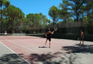 Fire personer spiller tennis på en udendørs bane omgivet af træer i Wecamp L'Escala Punta Mila, Catalonien.