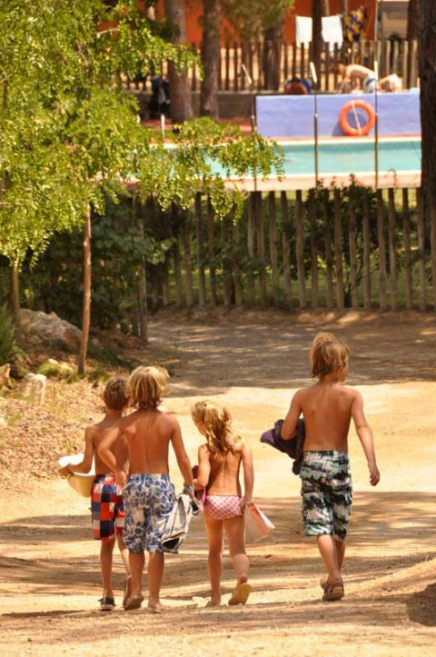 Cuatro niños en ropa de baño caminan hacia la piscina en Wecamp L'Escala Punta Mila, un parque de vacaciones en Cataluña.