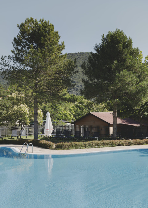 Piscine entourée de chaises longues, pins et montagnes à Wecamp Pirineos, parc de vacances en Aragón, Espagne.