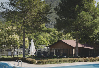 Zwembad met ligstoelen, dennenbomen en uitzicht op bergen bij Wecamp Pirineos vakantiepark in Aragón, Spanje.