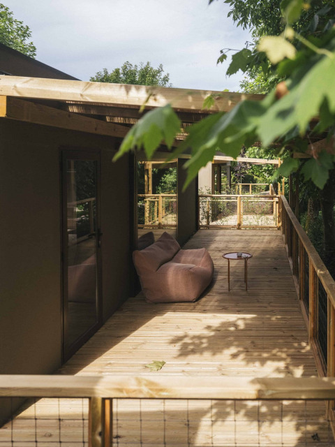 Terraza de madera con sofá y mesa en Wecamp San Sebastián, parque vacacional en el País Vasco, España, rodeada de árboles.