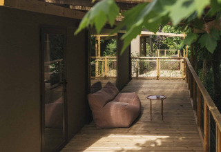 Terrasse en bois avec canapé et table au Wecamp San Sebastián, parc de vacances au Pays basque, Espagne, entouré d’arbres.