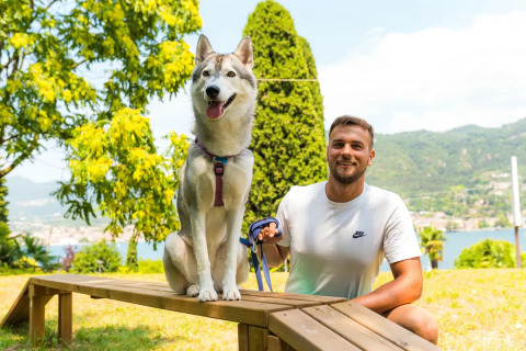 Man in a white t-shirt and his husky enjoying a sunny outdoor day at Weekend Glamping Resort, Lombardy, Italy.