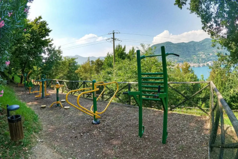Outdoor gym area with fitness equipment, lush greenery and scenic lake view at Weekend Glamping Resort, Italy.