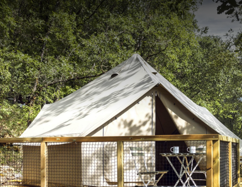 Safari-Bell-Zelt im Wald mit Holzterrasse, Tisch und zwei Tassen, ideal für entspannten Natururlaub.