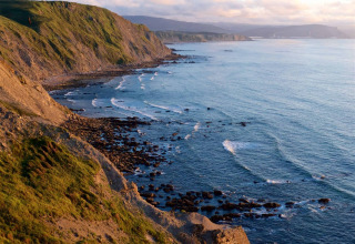Küstenlandschaft bei Cudillero in Asturien, Spanien, mit Felsen, Meer und einem fliegenden Vogel bei Sonnenuntergang.