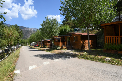Vue du lodge Mobile Home Basic Family avec cabanes en bois, arbres verts et montagnes à l’arrière-plan.