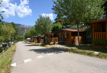 Blick auf Mobile Home Basic Family Lodge mit Holzhütten, grünen Bäumen und Bergen im Hintergrund.