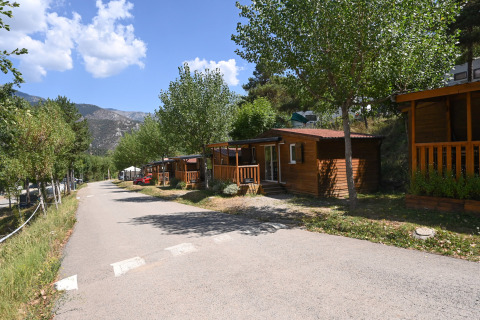 Vista del lodge Mobile Home Basic Family con casette di legno, alberi verdi e montagne sullo sfondo.