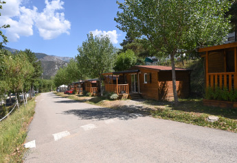Vista del lodge Mobile Home Basic Family con cabañas de madera, árboles verdes y montañas de fondo.