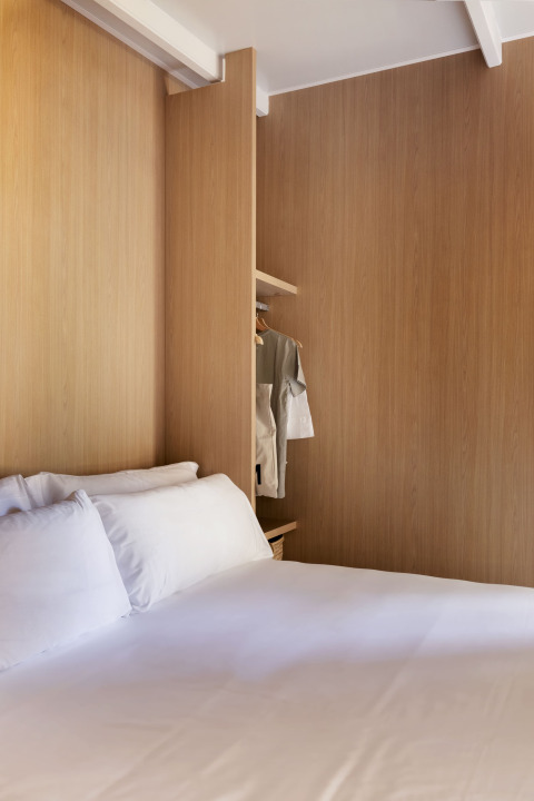 Glampingkamer met houten wandbekleding, wit beddengoed en een open kast met opgehangen kleding.