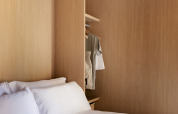 Glampingkamer met houten wandbekleding, wit beddengoed en een open kast met opgehangen kleding.