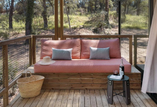 Terraza de madera con sofá rosa, cojines azules y cesta en Mobile home 'Couple Plus' en Wecamp San Sebastián, España.