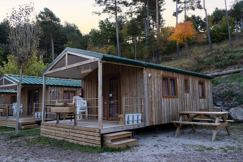 Houten chalets met veranda en picknicktafel bij Mobile Home Basic Family+ Panoramic, omgeven door natuur.