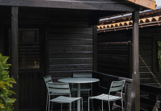 Pequeño porche de madera con mesa y tres sillas en Bungalow Basic Family Plus en Wecamp Cudillero, España.