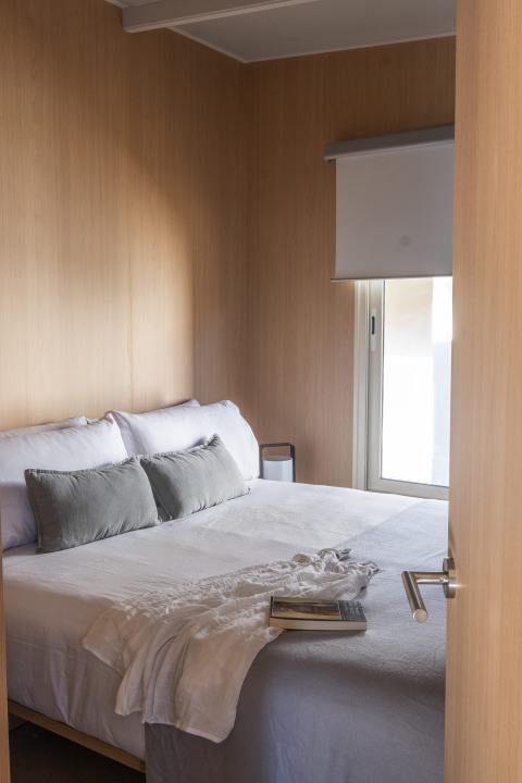Moderne glamping slaapkamer met houten wanden, comfortabel bed, kussens en boek op wit deken.