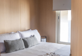 Modernes Glamping-Schlafzimmer mit Holzwänden, gemütlichem Bett, Kissen und Buch auf der Decke.