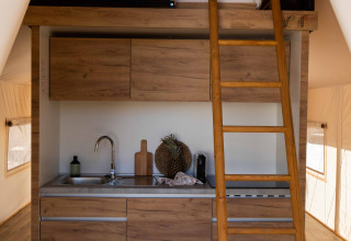 Interieur van een safaritent met een moderne kitchenette, houten ladder en slaapzolder bovenin.